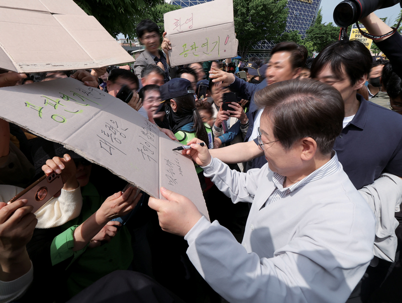 이재명 더불어민주당 대선후보가 5월7일 전북 전주시 풍남문 앞 광장에서 지지자가 든 ‘공판 연기 환영, 대통령은 국민이 뽑습니다’라는 팻말에 사인을 하고 있다. ⓒ연합뉴스